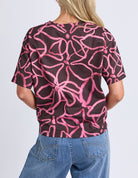 Person wearing a black t-shirt with pink abstract pattern and blue jeans on a white background