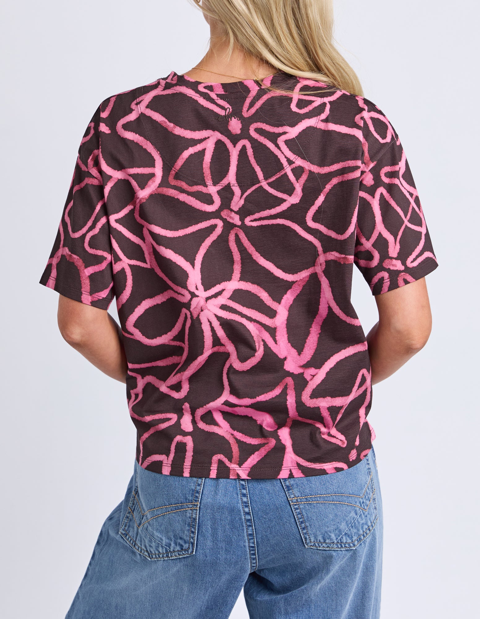 Person wearing a black t-shirt with pink abstract pattern and blue jeans on a white background