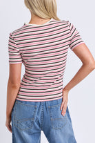 A woman shown from the back wearing a short-sleeve striped t-shirt with pink, black, and white horizontal stripes, paired with blue jeans, against a light gray studio background.