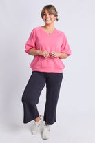 A woman modeling a pink crewneck sweatshirt and dark navy wide-leg pants against a light gray studio background.