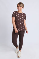 A woman modeling a brown short-sleeve t-shirt with white polka dots and matching brown leggings, paired with white sneakers, against a light gray studio background.