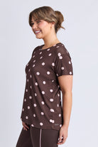 A woman wearing a brown short-sleeve athletic top with a white polka dot pattern, shown from a side profile against a light gray studio background.