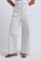 A person wearing off-white wide-leg cropped jeans with a white top and dark flip-flops, shown from the waist down against a light gray studio background.