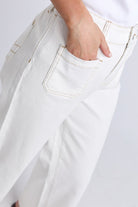 Close-up of a person wearing off-white or cream-colored jeans, showing the back pocket with a hand in the pocket and light contrast stitching.