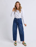 Woman wearing blue jeans and a white shirt on a plain background