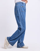 A person wearing blue wide-leg jeans and white sneakers, shown from the waist down in a side-profile pose against a clean white studio background.