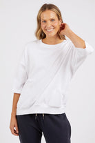 Woman wearing a white oversized sweater and dark pants on a light background