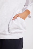 Person wearing a white sweatshirt with a pocket, standing against a plain background