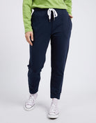 Person wearing navy jogger pants with a green top and white sneakers on a light gray background