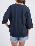 A person shown from the back wearing an oversized dark navy blue short-sleeve top and light blue denim shorts against a plain light gray studio background.
