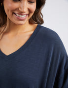 Close-up of a woman wearing a navy blue V-neck top, showing the fabric texture and neckline detail against a light gray background.