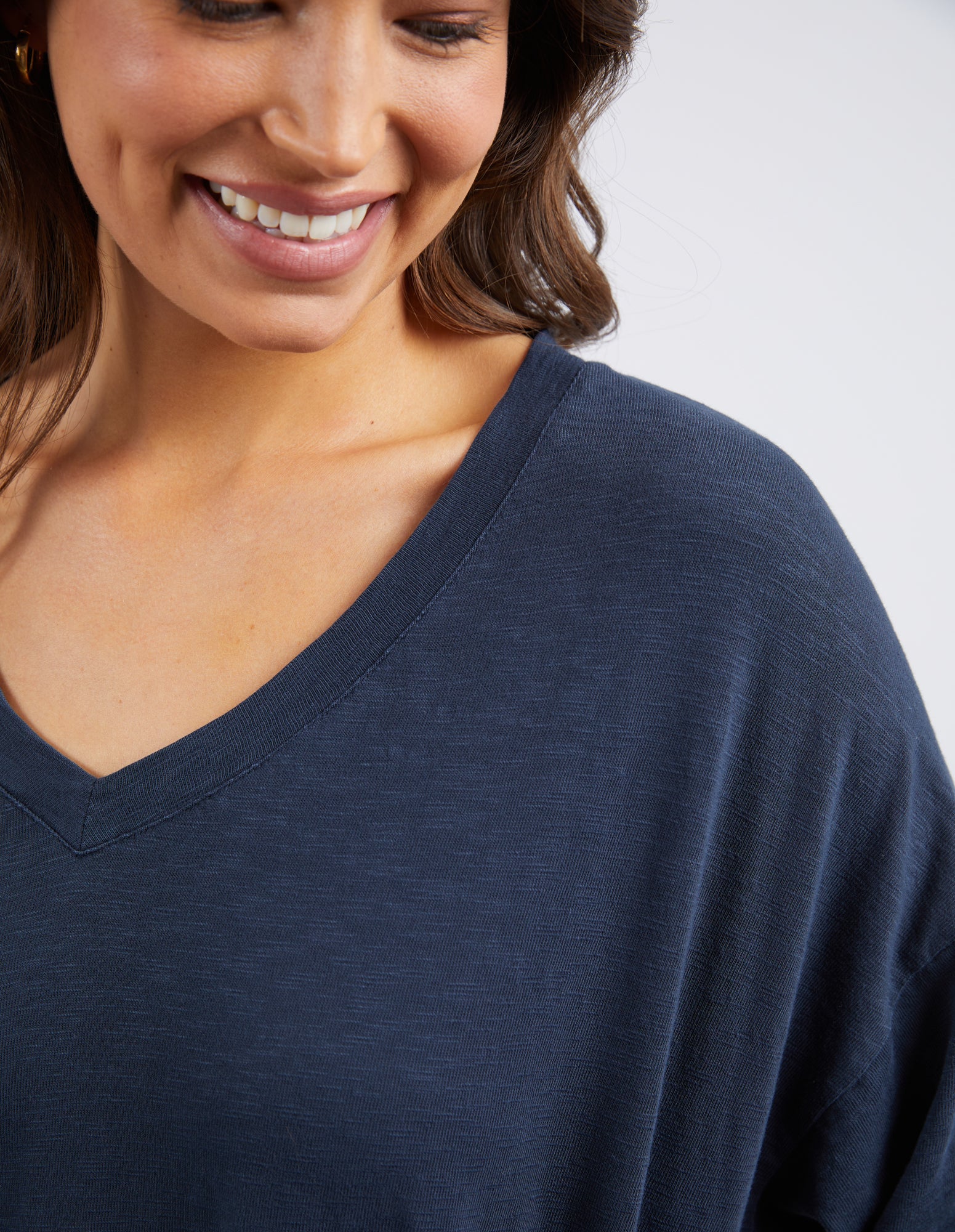 Close-up of a woman wearing a navy blue V-neck top, showing the fabric texture and neckline detail against a light gray background.