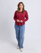 Woman wearing a red long-sleeve top and blue jeans on a white background