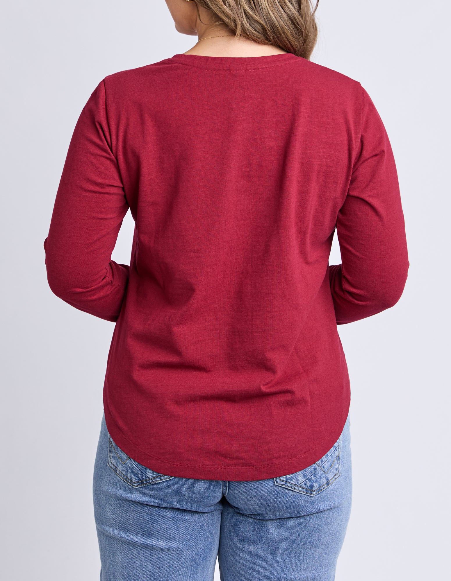 Person wearing a red long-sleeve shirt and blue jeans on a light gray background