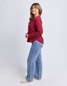 Woman wearing a red long-sleeve top and blue jeans on a white background