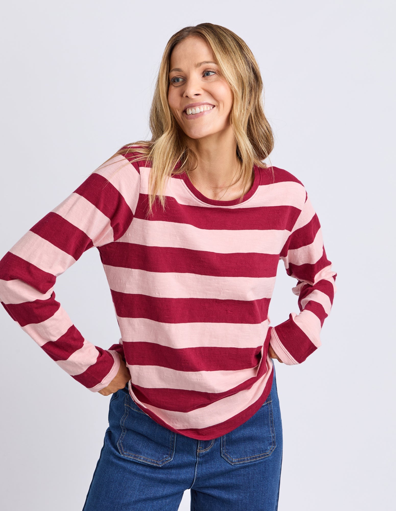 Woman wearing a red and pink striped sweater with blue jeans on a light gray background