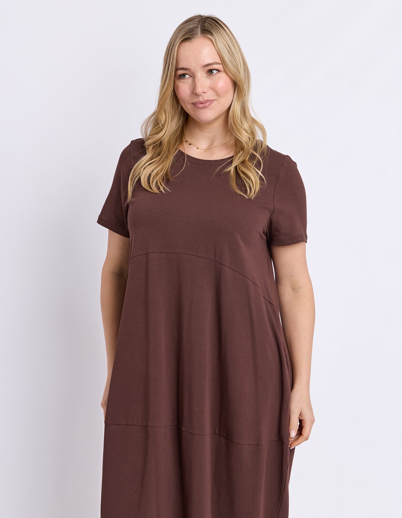 A woman modeling a short-sleeve, crew-neck dress in a solid dark brown color, photographed against a light gray studio background.