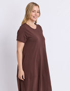 A woman modeling a short-sleeve, crew-neck, tiered maxi dress in a solid dark brown color, photographed against a clean, light gray studio background.