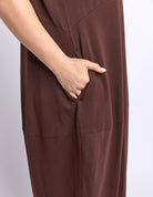 Close-up of a person wearing a brown wide-leg garment with a side pocket, showing the hand inserted into the pocket against a light gray background.