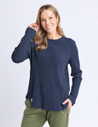 Woman wearing a navy blue sweater and green pants on a white background