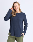 Woman wearing a navy blue sweater and green pants on a white background