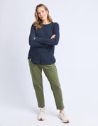 Woman wearing a navy sweater and green pants on a white background