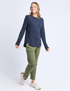 Woman wearing a navy sweater and green pants on a white background