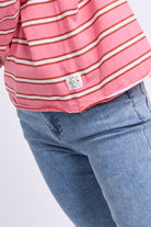 Close-up of a pink and white striped shirt worn with blue jeans, showing the side seam and a small triangular brand patch near the hem.