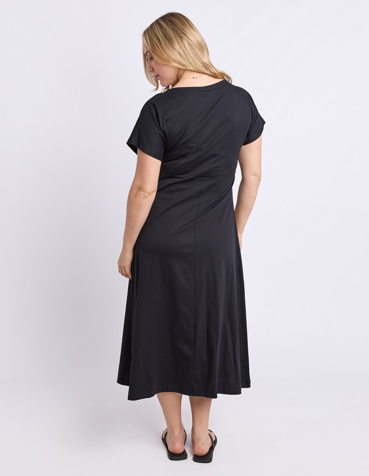 A woman modeling a black short-sleeve midi dress from the back, shown against a plain light gray studio background.