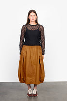Woman wearing a black top with sheer sleeves and a brown skirt against a white background
