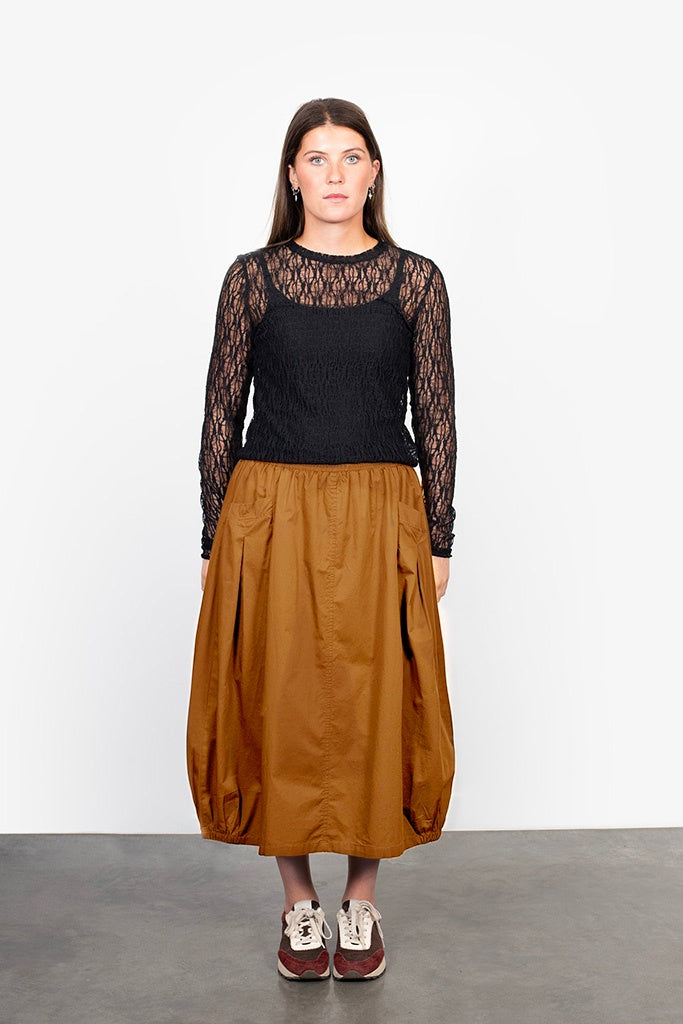 Woman wearing a black top with sheer sleeves and a brown skirt against a white background