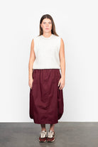 Woman wearing a white sleeveless top and burgundy skirt against a white background
