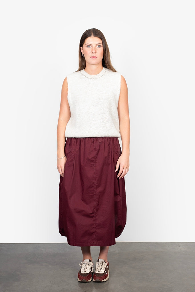 Woman wearing a white sleeveless top and burgundy skirt against a white background