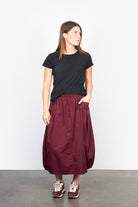 Woman wearing a black t-shirt and burgundy skirt on a plain background