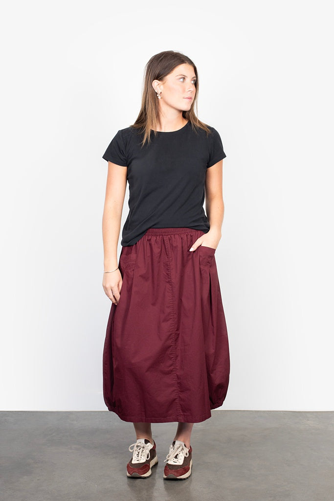 Woman wearing a black t-shirt and burgundy skirt on a plain background