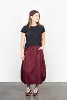 Woman wearing a black t-shirt and burgundy skirt on a plain background