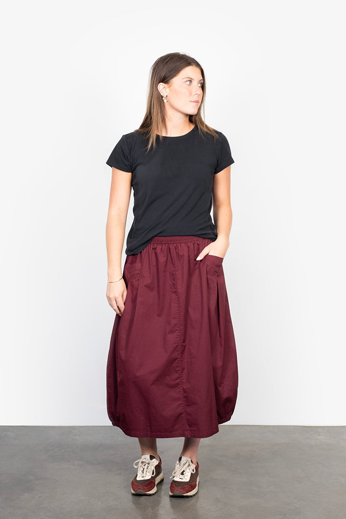 Woman wearing a black t-shirt and burgundy skirt on a plain background