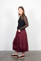 Woman wearing a black lace top and burgundy skirt against a white background