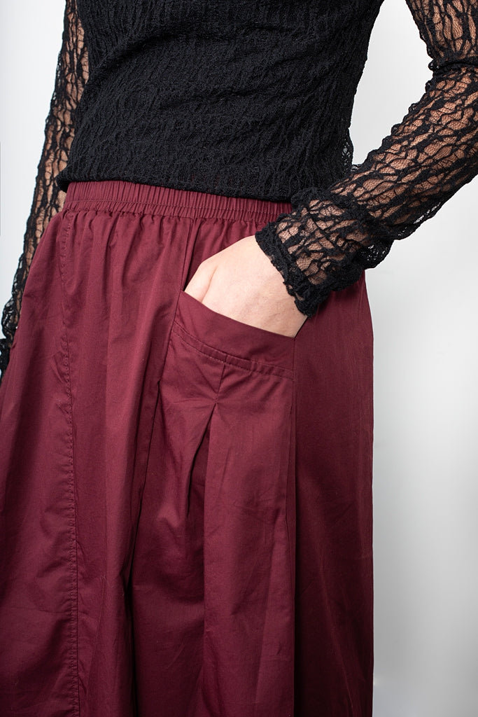 Person wearing burgundy pants with a black textured top and lace sleeves.