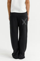 Person wearing black pants with a large 'X' logo on a white background