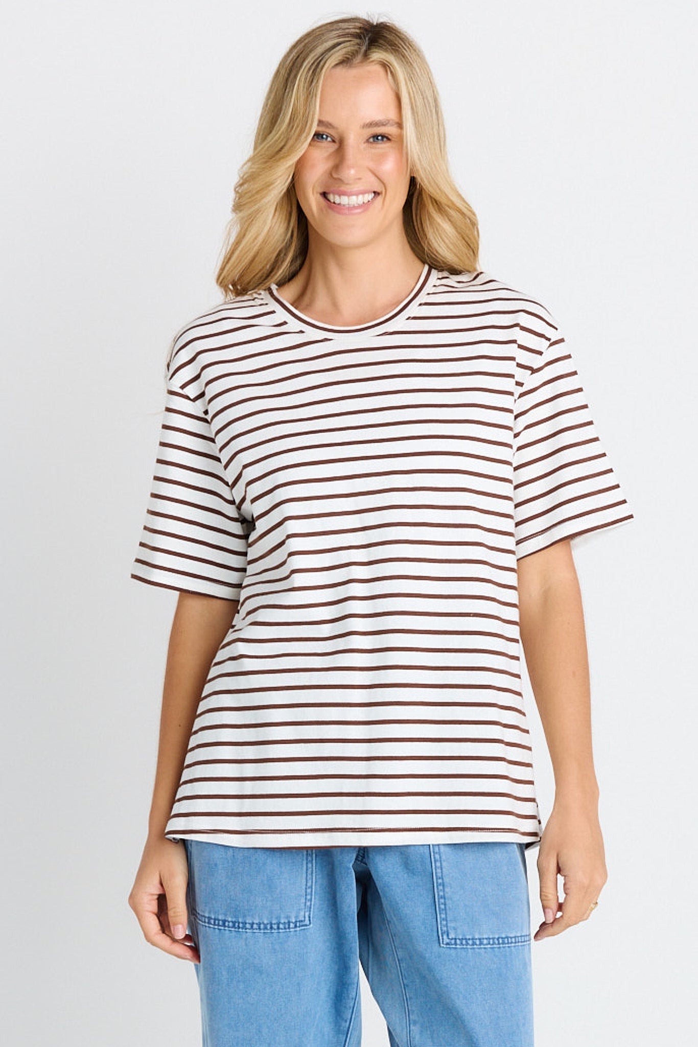 Woman wearing a striped shirt and blue jeans on a plain background