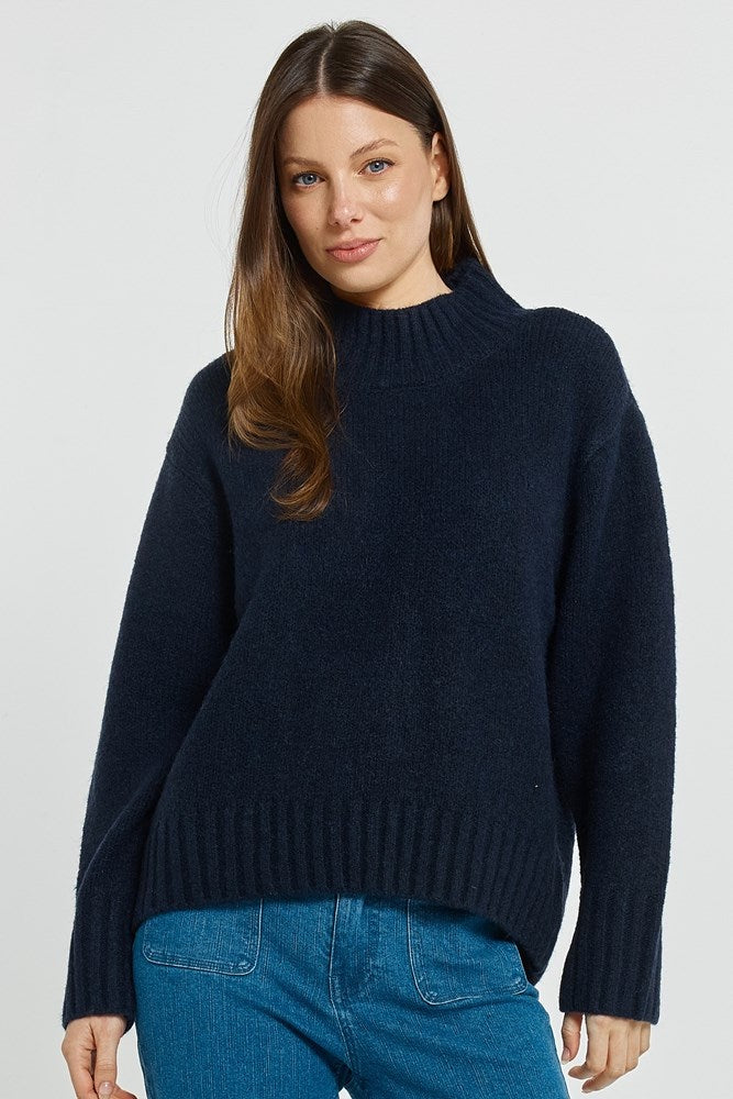 Woman wearing a navy sweater and blue jeans on a light gray background
