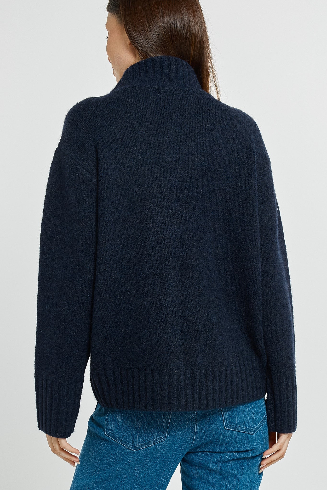 Person wearing a navy sweater and blue jeans on a light gray background
