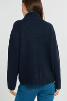 Person wearing a navy sweater and blue jeans on a light gray background