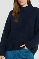 Person wearing a dark blue sweater and blue jeans on a light gray background