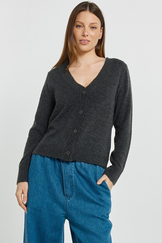 Woman wearing a dark gray cardigan and blue pants on a light gray background
