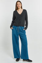 Woman wearing a dark gray cardigan and blue pants on a white background