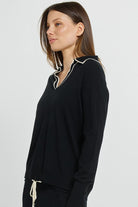 Woman wearing a black long-sleeve top with white trim on a light gray background