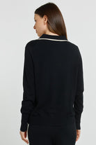 Woman wearing a black long-sleeve top with white trim on a light gray background
