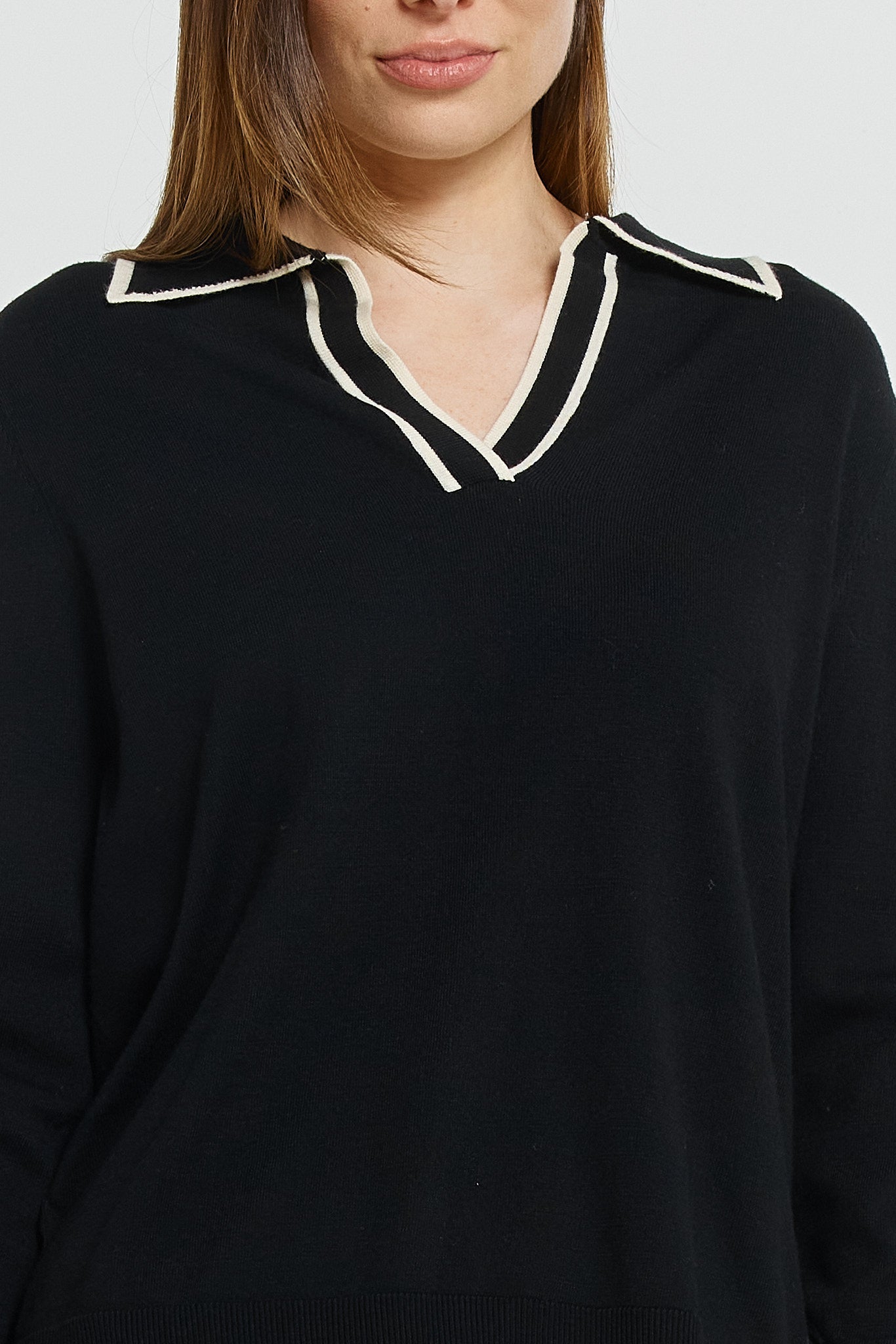 Black sweater with white trim worn by a person on a light gray background